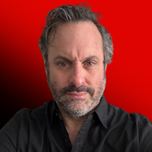 Portrait of a man with dark hair and stubble wearing a black shirt, against a red-to-black gradient background.