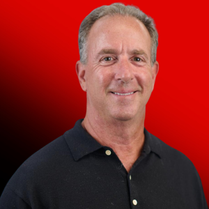 Portrait of a smiling middle-aged man in a dark polo shirt, against a red gradient background.