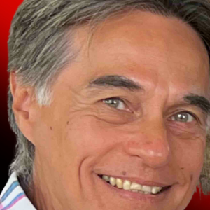 Close-up portrait of a smiling middle-aged man with gray hair against a red background, showing a friendly expression.