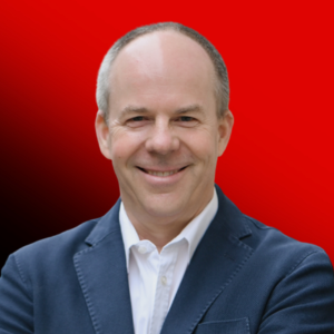 Smiling man in a navy blazer and white shirt, head-and-shoulders portrait against a red gradient background.