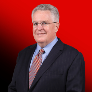 Professional portrait of an older man with gray hair and glasses, wearing a dark pinstripe suit and red tie, against a red gradient background.