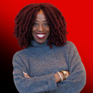 Smiling woman with curly red hair wearing a blue sweater, arms crossed, against a red gradient background.